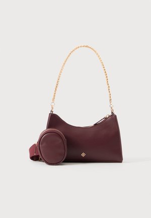 Sac à main bordeaux foncé avec une anse chaîne dorée et une pochette ronde détachable assortie sur fond uni.