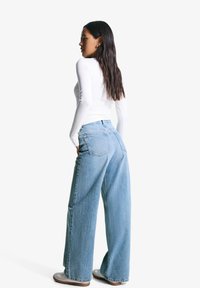 Jean large bleu clair avec taille haute, délavé, et deux poches arrière, associé à un haut blanc à manches longues.