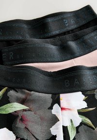Tissu à motif floral avec une bande noire, comportant un texte en relief "BAKER par TED BAKER". Des tons roses doux et sombres sont visibles dans le design.
