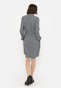 Langärmliges Kleid mit schwarzem Grund und weißem Blumenmuster, mit einem leicht ausgestellt geschnittenen Saum und versteckten Seitentaschen. Getragen mit schwarzen Ankle Boots.