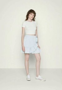 Saia envolvente azul clara com uma barra franzida, segura por um nó atado. Combinada com uma t-shirt branca corta e ténis brancos.