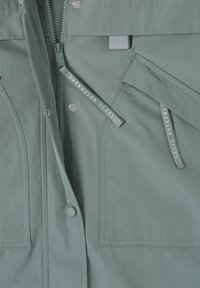 Veste vert clair avec fermeture éclair frontale, boutons-pression et deux poches latérales rectangulaires avec languettes en tissu étiquetées "CECIL OUTERWEAR".