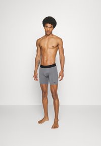Grå sportshorts med ett svart elastiskt midjeband och en liten svart logotyp. Shortsen har en slät textur och en figurnära design.