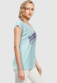 Lys blå t-skjorte med korte ermer og v-hals, med et trykt "Park Fields"-logo i marineblått. Stoffet ser mykt ut med en glatt tekstur.