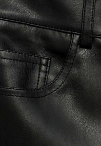 Tessuto in pelle sintetica nera con superficie texturizzata, cuciture visibili e outline di una piccola tasca per dettagli di design.