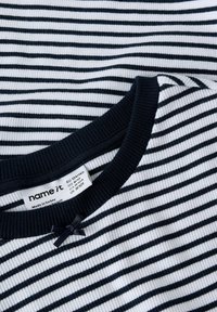 Top de rayas con canalé en blanco y azul marino, con un escote azul marino y un pequeño detalle de moño. La etiqueta indica la talla y la información de fabricación.