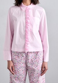 Light pink shirt with a ruffled front and long sleeves, paired with floral-patterned pants featuring multicolored blossoms on a white background.