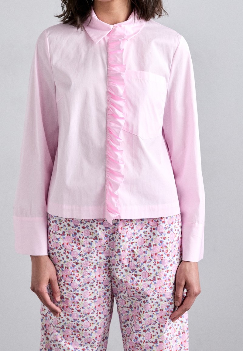 Light pink shirt with a ruffled front and long sleeves, paired with floral-patterned pants featuring multicolored blossoms on a white background.