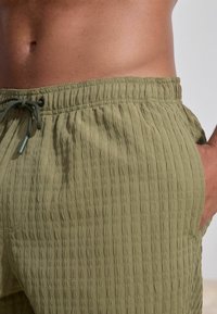 Olivgrüne Shorts aus strukturiertem Stoff, mit einem gerippten Muster, elastischem Taillenbund und Kordelzugdetail.