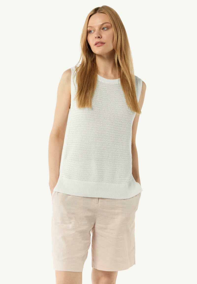 Weißes ärmelloses Stricktop mit einem strukturierten Muster und einem runden Halsausschnitt, kombiniert mit hellbeigen Leinen-Shorts.