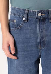 Jeans de mezclilla azul claro con un diseño clásico de cinco bolsillos, cierre de botón y detalles de costura en contraste en las costuras.