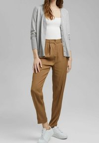 Jasnoszary kardigan na białym topie na ramiączkach, w połączeniu z brązowymi, wysokim stanem spodniami i białymi trampkami. Gładkie faktury i dopasowany krój.