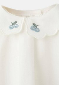 Bela bluza z obrobo v valovih z modro vezenino jagod in zelenih listov. Iz mehke, lahke tkanine.