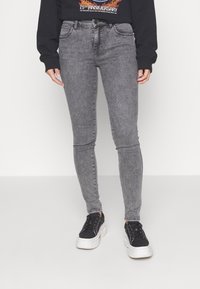 Jeans skinny de mezclilla gris con un acabado desgastado, cinco bolsillos y pasadores para cinturón, combinados con zapatillas negras y un sudadera gráfica negra.