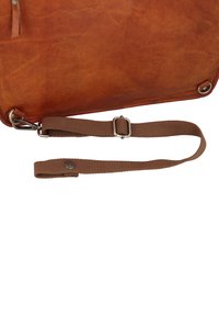 Braune Ledertaschenecke mit angebrachtem verstellbarem braunem Stoff-Schultergurt und Metallschnalle auf weißem Hintergrund.