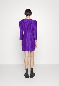 Lila klänning med strukturerad mönster, trekvartsärmar och figurnära siluett. Bärs med svarta ankelboots med kraftiga sulor.