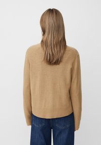Beige Wollpullover mit einem gerippten Saum, langen Ärmeln und einer lockeren Passform. Dunkelblaue Jeans mit sichtbaren Gesäßtaschen.