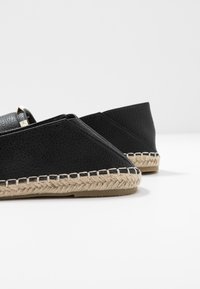 Espadrilles en cuir noir avec une finition texturée, dotées d'une semelle en jute tissée et d'accents métalliques à l'avant.