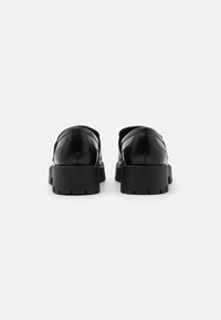 Sorte lærskor med en blank finish, tykke gummisåler og et strømlinjeformet design, med avrundede kanter og minimale sømdetaljer.
