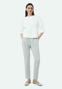 Witte gestructureerde pullover, grijze tapered broek en zilveren platte schoenen. Zachte materialen, casual ontwerp en minimale accenten.