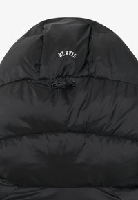 Veste en duvet noire avec une texture matelassée, présentant un logo de marque "BLKVIS" et un cordon de serrage réglable au col.