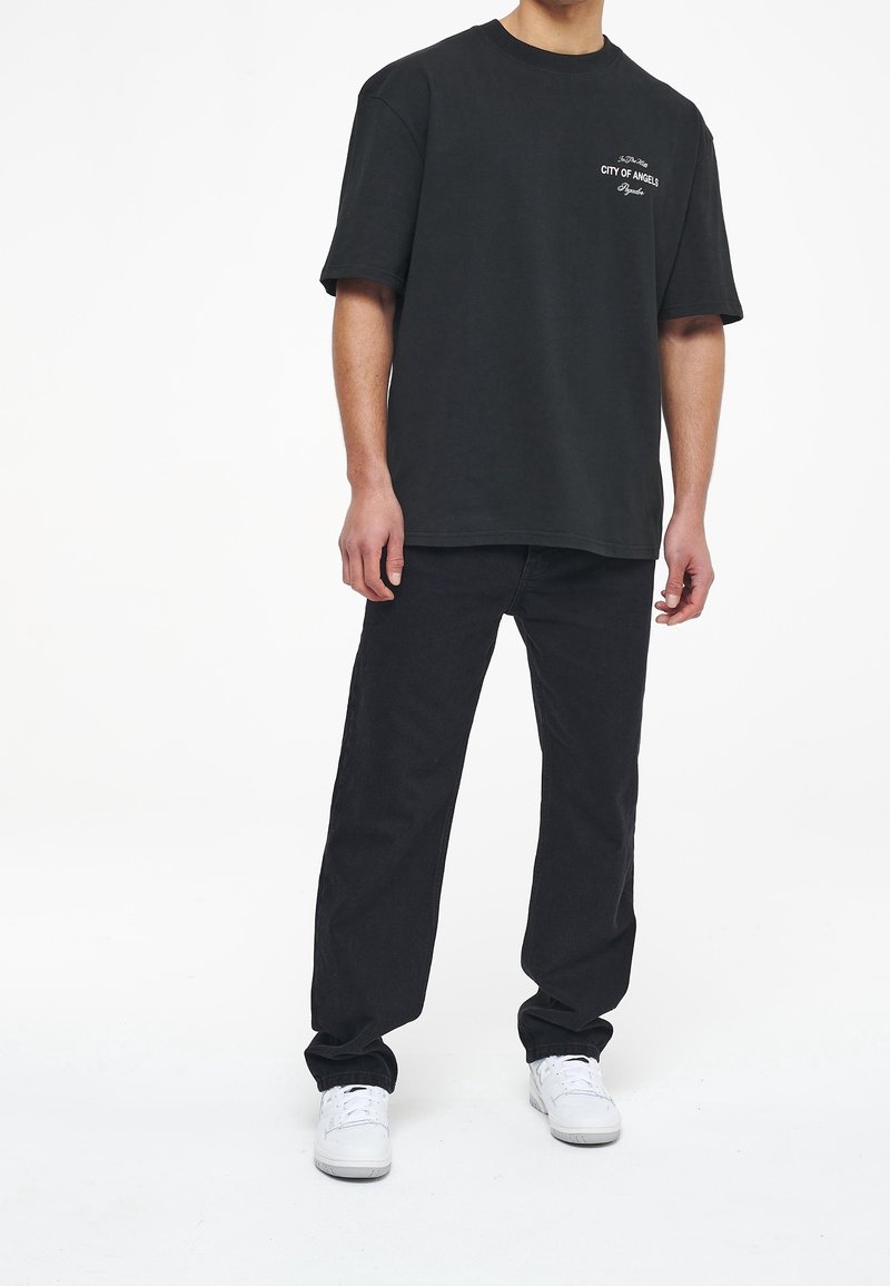 Černé oversized tričko s textem "MĚSTO ANDĚLŮ", kombinované s černými denimovými kalhotami a bílými teniskami. Jednoduchý design a pohodlný střih.