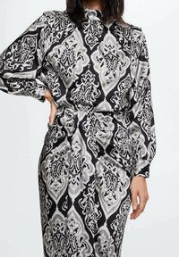 Robe à motifs noirs et gris avec un col montant, des manches longues et une taille cintrée, présentant un design complexe et une texture douce.