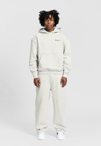 Ljusgrå hoodie med kenguruficka och logotyp framtill, i kombination med matchande vida sweatpants. Mjuk bomullsblandning, avslappnad passform.