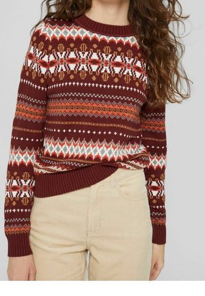 Pull en tricot rouge avec des motifs géométriques en blanc et orange, doté d'un col rond et d'une bordure côtelée. Associé à un pantalon en velours côtelé beige.