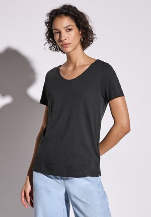 Camiseta negra de manga corta con escote redondeado, hecha de material suave, con un ajuste relajado y costuras en los hombros, combinada con jeans claros.