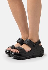 Sandales à plateforme noires avec deux larges brides, boucles réglables, semelle texturée et design ouvert à l'avant. Fabriquées en matériau synthétique.