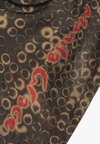 Sciarpa di seta nera con motivo circolare beige e testo rosso. Il tessuto ha una consistenza liscia, drappeggiandosi elegantemente con una leggera lucentezza.