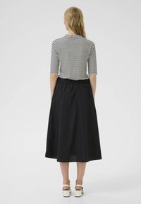 Falda midi negra, fruncida, combinada con una blusa a rayas de mangas tres cuartos. La blusa tiene un escote con ondas y una textura de tela ligera.