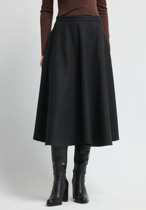 Zwarte A-lijn rok van gestructureerde stof, met een hoge taille en plooien, gecombineerd met zwarte leren laarzen tot de knie.
