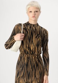 Schwarzes und goldenes Langarmkleid mit Tigerstreifenmuster, hochgeschlossenem Kragen und gerafftem Taillenbereich. Begleitet von einer weißen Tasche.