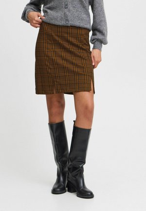 Jupe en tartan marron avec une fente sur le côté, tissu texturé, portée avec un cardigan gris et des bottes en cuir noir jusqu'aux genoux.