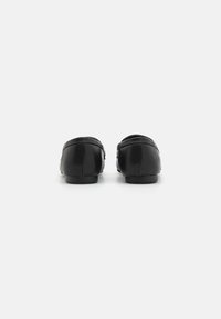 Mocassins en cuir noir avec une texture lisse, bout rond et petit talon ; présentent des coutures visibles et un design simple et discret.
