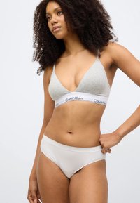 Γκρι τριγωνικό σουτιέν από βαμβάκι με λεπτές τιράντες και λευκή ταινία με τη φράση "Calvin Klein." Λευκό αδιάβροχο εσώρουχο hipster χωρίς ραφές.