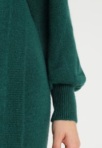 Pull vert en tricot avec poignets côtelés et finition texturée, doté d'une coupe décontractée et de manches légèrement bouffantes.
