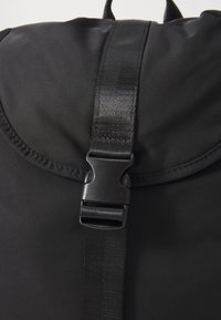 Black backpack featuring a smooth nylon material, a rounded flap closure, and a glossy plastic buckle strap for secure fastening.