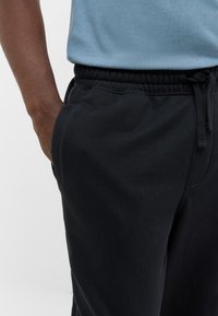 Schwarze Jogginghosen aus weichem Stoff mit elastischem Bund, ausgestattet mit Seitentaschen und einem Kordelzugverschluss zur Anpassung.