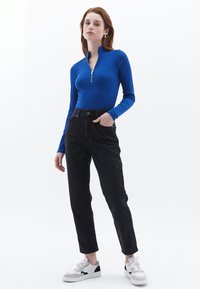 Koninklijkblauwe lange mouw zip-up top met een slim fit, gecombineerd met hoge zwarte rechte jeans en witte sneakers met zwarte accenten.