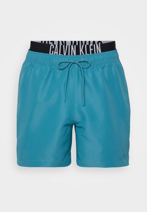 Turquoise zwembroek met een zwarte elastische tailleband voorzien van witte "CALVIN KLEIN" letters en een verstelbaar trekkoord.