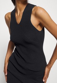 Robe noire sans manches en maille, dotée d'un col en V et d'un motif texturé. Coupe ajustée avec des coutures définies et une finition lisse.