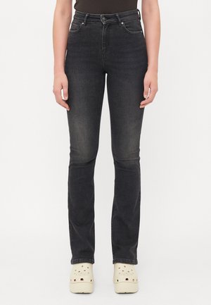 Jean noir taille haute à coupe slim, avec cinq poches, un léger effet délavé et des coutures contrastées, associés à des sabots crème.