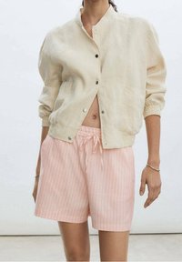 Veste bomber en lin beige clair avec fermeture à pression et poignets élastiques, assortie à un short rayé rose clair avec cordon de serrage.