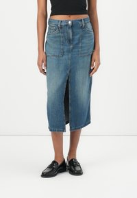 Lys blå denim midi-skirt med frontslit, to frontlommer og belte med knappeåpning. Glatt tekstur. Svarte loafers.