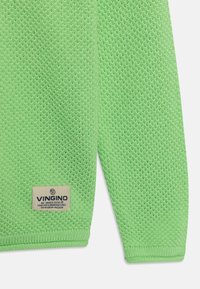 Zelený pletený svetr s texturovaným vzorem. Má žebrované manžety a lem. Na dolním levém rohu je viditelná štítka s názvem značky.