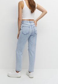 Jeans in denim azzurro chiaro a vita alta con dettagli usurati, design a cinque tasche e vestibilità rilassata, abbinati a sneakers bianche.