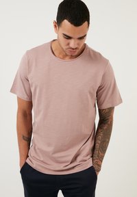 Tricou cu mânecă scurtă și guler rotund, de culoare mauve deschis, realizat dintr-un material moale, cu o textură netedă și o croială lejeră. Nu are logo-uri vizibile.